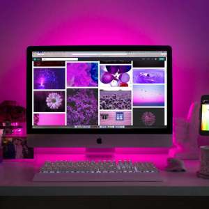 Modern desk setup with neon lighting and a desktop computer displaying colorful images.
